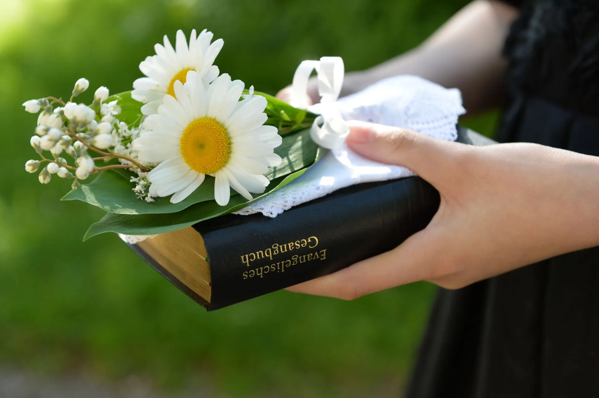 Konfirmandin mit Gesangbuch und Blumen.