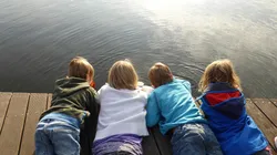 Vier Kinder liegen auf Steg und beobachten das Wasser